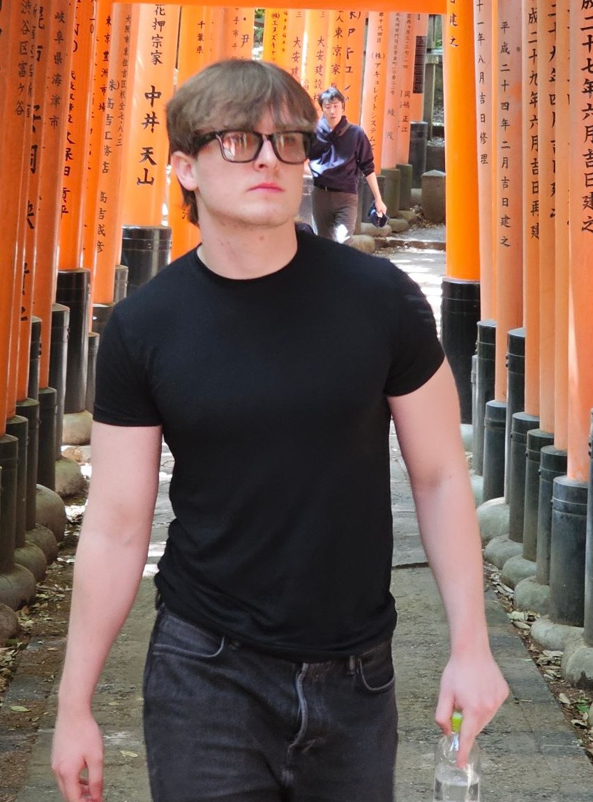 Jake walking through the orange torii gates at Fushimi Inari in Japan, in a black t-shirt and glasses