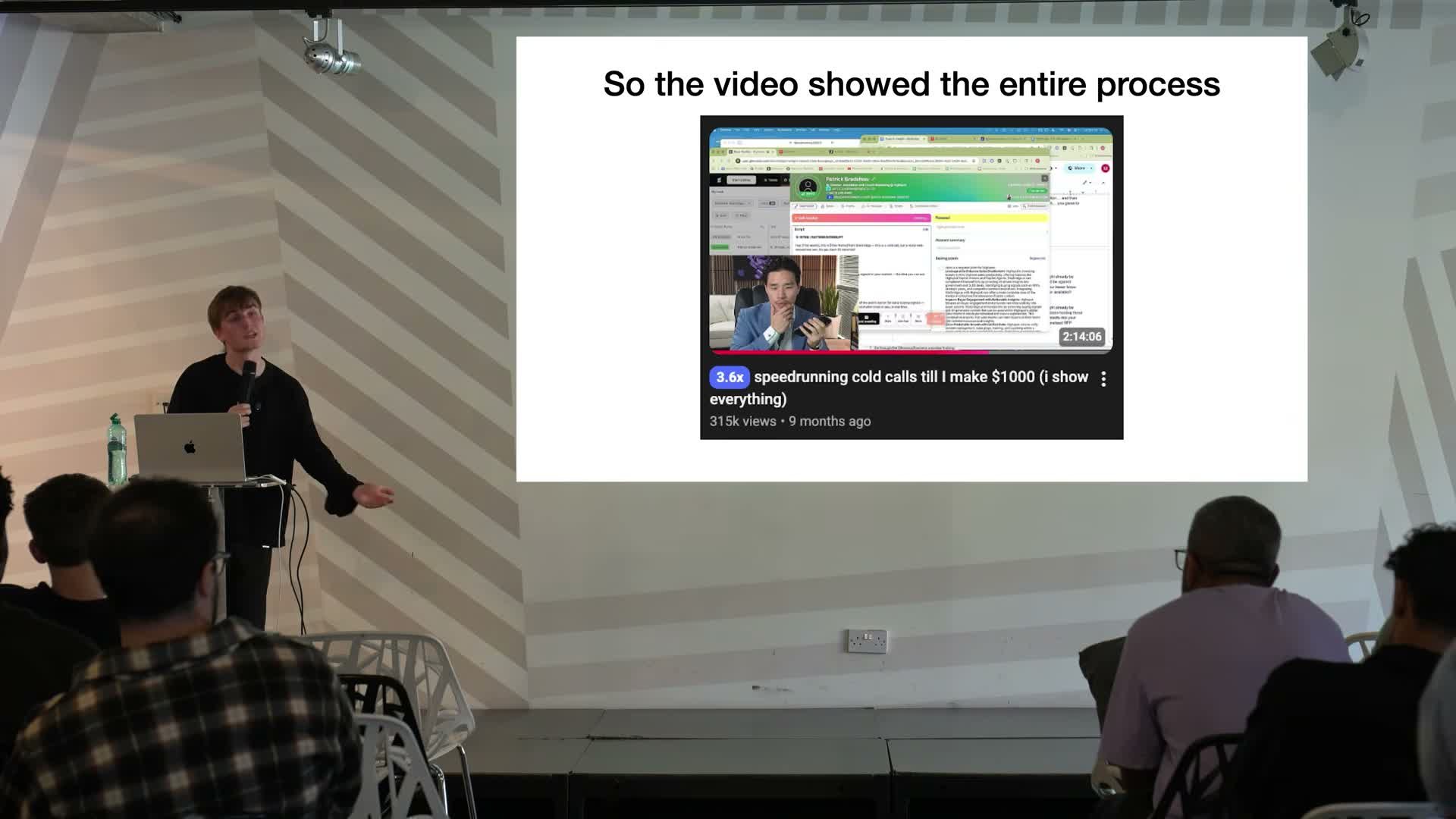 Jake Trinder at a lectern answering audience questions in front of a slide